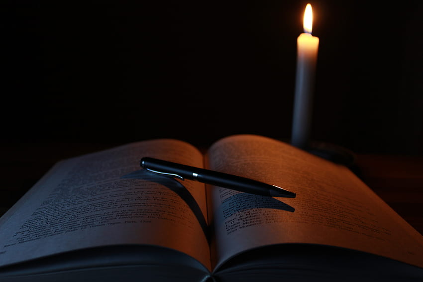 Czarny długopis na otwartej książce obok zapalonej świecy stożkowej · Tapeta HD