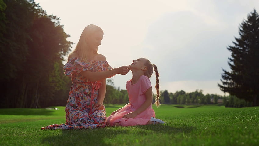 Fröhliche Familie albert bei Sonnenuntergang im Stadtpark herum. Lächelnde Frau spielt mit Mädchen im Freien. Fröhliche Mutter kitzelt Tochter auf grünem Gras auf der Wiese. Stockvideomaterial, fröhliche Wiese HD-Hintergrundbild