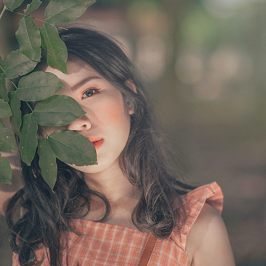 Selektive Fokusgrafik einer Frau im orangefarbenen ärmellosen Oberteil, das das Gesicht hinter dem Blatt des Baums verbirgt · Auf Lager, Mädchengesicht verstecken HD-Handy-Hintergrundbild