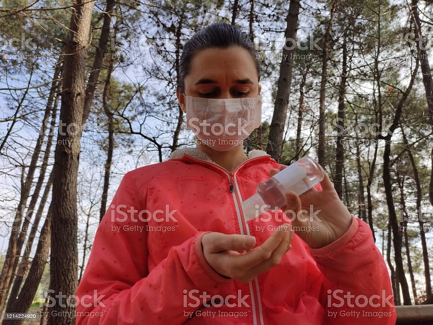 Frau im Wintermantel mit Schutzmaske im Gesicht und Händedesinfektionsmittel HD-Hintergrundbild