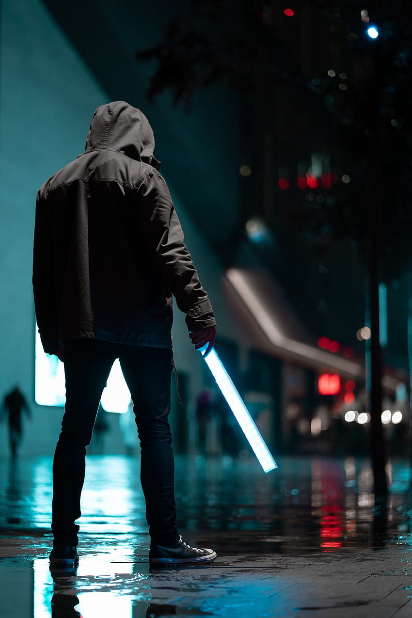 Mężczyzna w czarnej bluzie z kapturem stojący nocą na betonowym chodniku · Tapeta na telefon HD