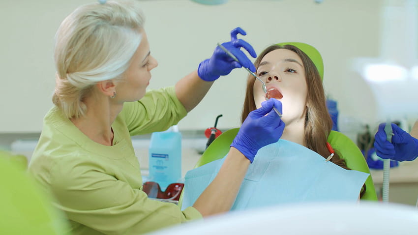 Зъболекар преглежда зъбите на пациента със зъболекарски инструменти. Лекар и пациент в модерен интериор на стоматологична клиника. Професионални процедури за устна хигиена на стоматологичен стол. Ежектор за слюнка в отворената уста на пациента Стоков видеозапис HD тапет