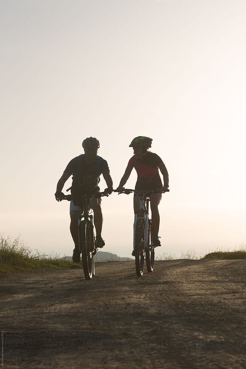 Pareja joven montando en bicicleta en una carretera rural durante la puesta de sol, pareja de jinetes fondo de pantalla del teléfono
