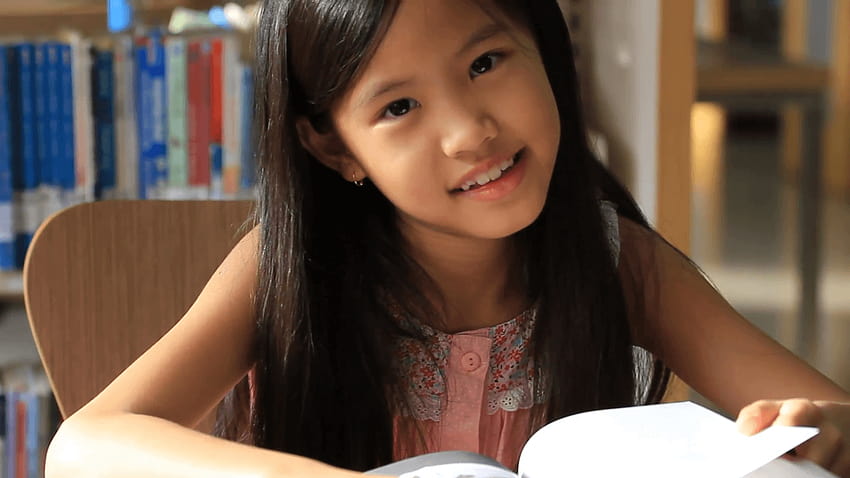 Kleines asiatisches Mädchen, das ein Buch in der Bibliothek liest, Pan Shot Stock Video Footage HD-Hintergrundbild