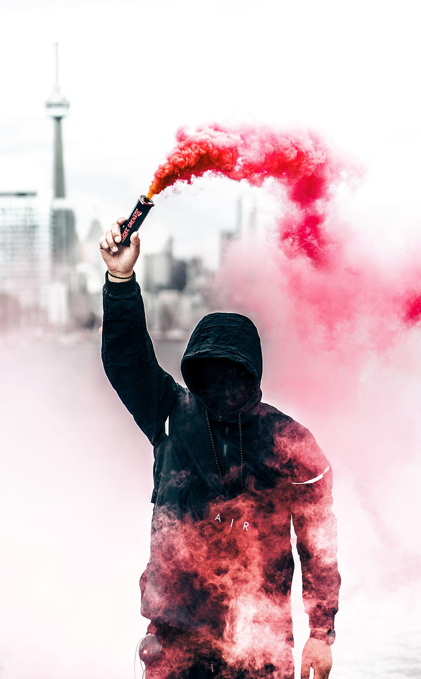 顔を隠した黒いパーカーを着た人がピンク色の煙、発煙弾を掲げている HD電話の壁紙