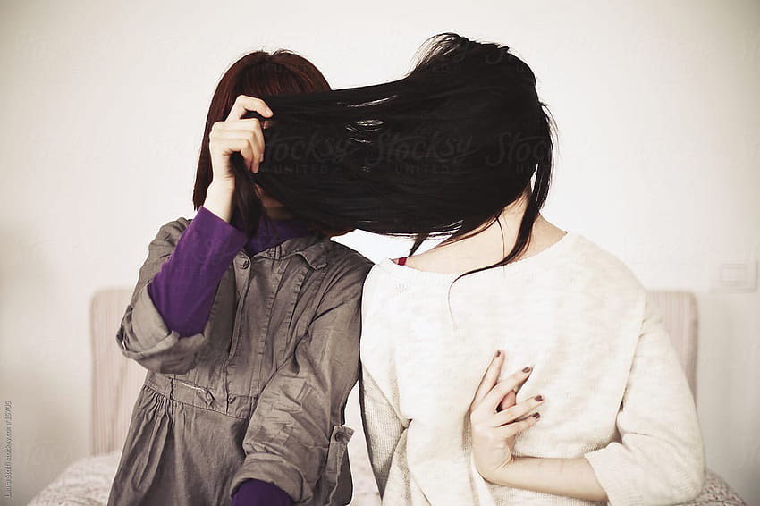 Two girls, one hiding her face with hair, the other seen from the back while sitting on bed by Laura Stolfi, hide faces pic HD wallpaper
