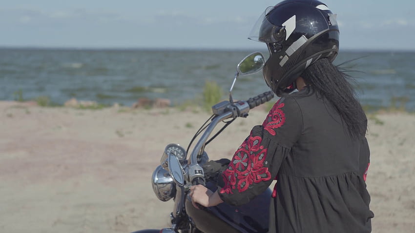 Menina caucasiana usando vestido preto e capacete sentado na motocicleta olhando para a câmera. Hobby, viajar e estilo de vida ativo. Motociclista em sua moto ao ar livre. Lazer e viagens de moto. Estoque de vídeo papel de parede HD