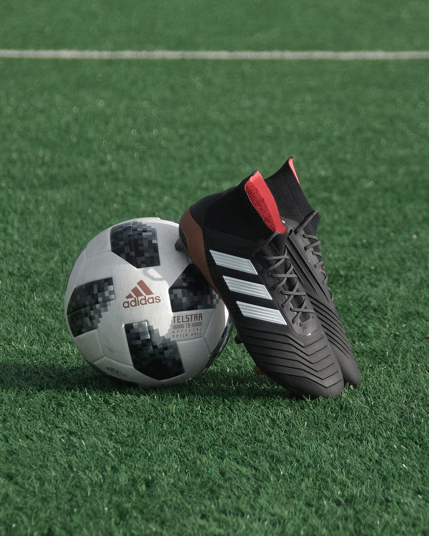 Schwarze adidas-Stollenschuhe stützen sich auf weißen und schwarzen adidas-Fußball auf grünem Gras – Fußball HD-Handy-Hintergrundbild