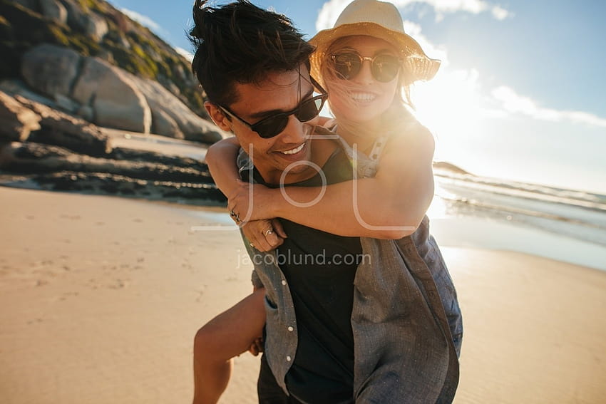 Fidanzato che fa un giro sulle spalle alla fidanzata in spiaggia – Jacob Lund graphy Store Sfondo HD