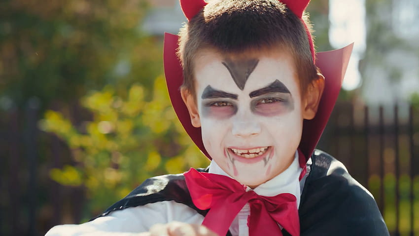 Potret anak laki-laki kecil yang lucu mengenakan riasan dan kostum halloween dengan tanduk setan dan jubah tersenyum dan mencoba untuk bertindak menakutkan Stok Rekaman Video Wallpaper HD
