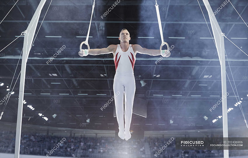 Ginnasta maschile in equilibrio con le braccia tese su anelli di ginnastica in arena, ginnasta ad anello Sfondo HD