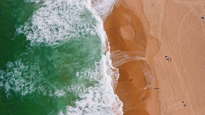 Top aerial view of waves break on tropical yellow sand beach. Bird's eye perspective of emerald green ocean surface and tourist laying in sum and relaxing on holiday Stock Video Footage, aerial view beach sand and ocean waves HD wallpaper