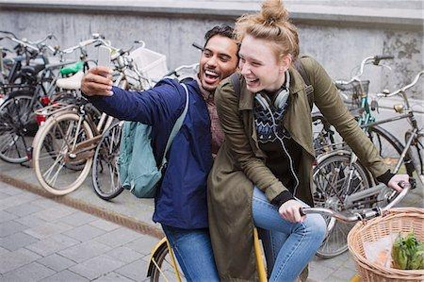 Pareja joven juguetona y riendo tomando selfie con teléfono con cámara en bicicleta Stock, biker selfie fondo de pantalla