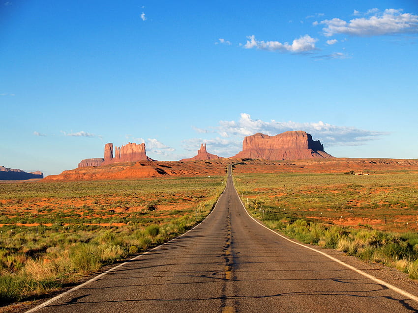 Carretera asfaltada en medio del campo de hierba bajo el cielo azul, parque tribal navajo del valle del monumento fondo de pantalla