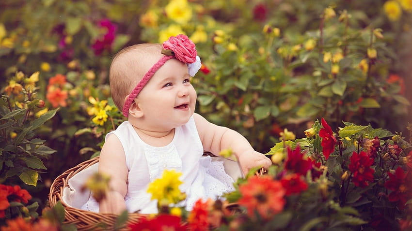 เด็กผู้หญิงยิ้มน่ารักนั่งอยู่ในตะกร้าไม้ไผ่ล้อมรอบด้วยดอกไม้หลากสีสวมชุดสีขาวและดอกไม้คาดศีรษะ น่ารัก วอลล์เปเปอร์ HD
