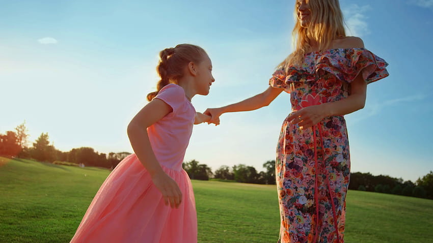 Feliz madre e hija bailando en un prado verde. Mujer alegre con una chica adorable disfrutando del atardecer al aire libre. Familia alegre tomados de la mano en el parque de la ciudad. Stock Video Footage, prado alegre fondo de pantalla