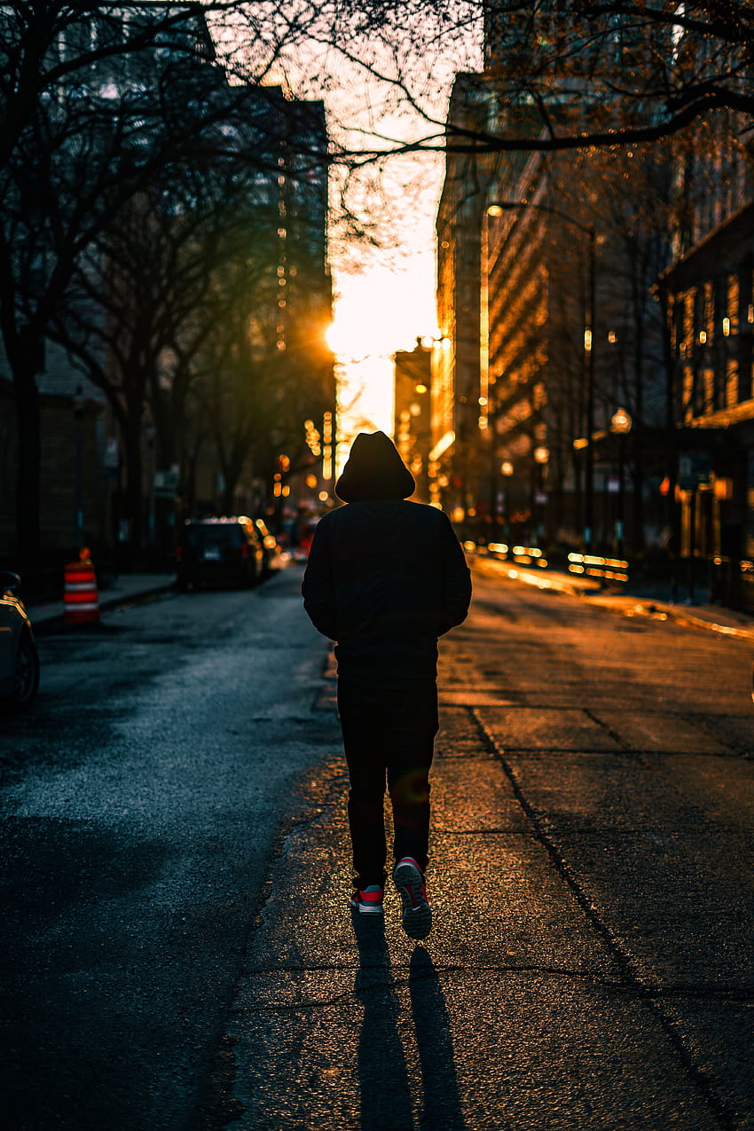 persona con capucha negra caminando por la calle durante la hora dorada, niño caminando fondo de pantalla del teléfono