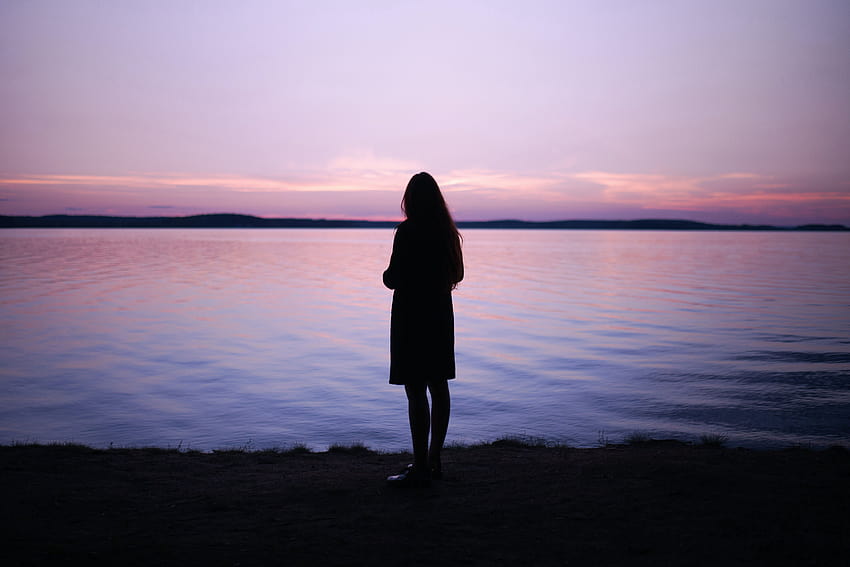 Frau, die während der goldenen Stunde in der Nähe eines Gewässers steht – allein Schatten HD-Hintergrundbild