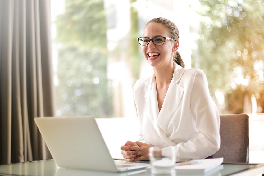 Lachende Geschäftsfrau, die im Büro mit Laptop arbeitet · Lager, Büroverwaltung HD-Hintergrundbild