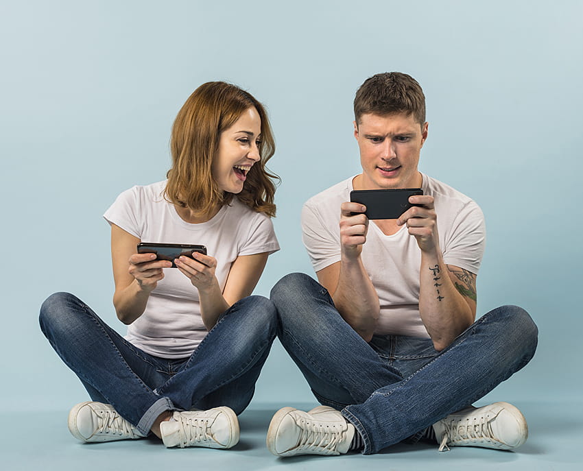Los teléfonos inteligentes de cabello castaño Man Laughter juegan con 2 mujeres jóvenes, hombres y mujeres sentados juntos fondo de pantalla